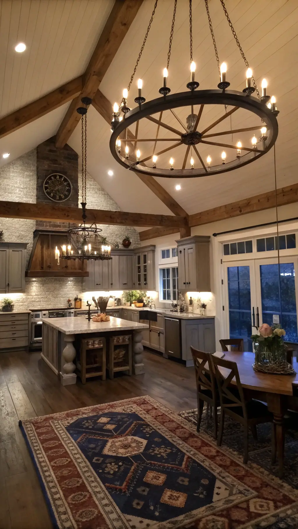Twilight view of a spacious kitchen-dining area with vaulted ceiling, wrought iron chandelier, gooseneck sconces, lantern pendants, and vintage rug over oak planks.