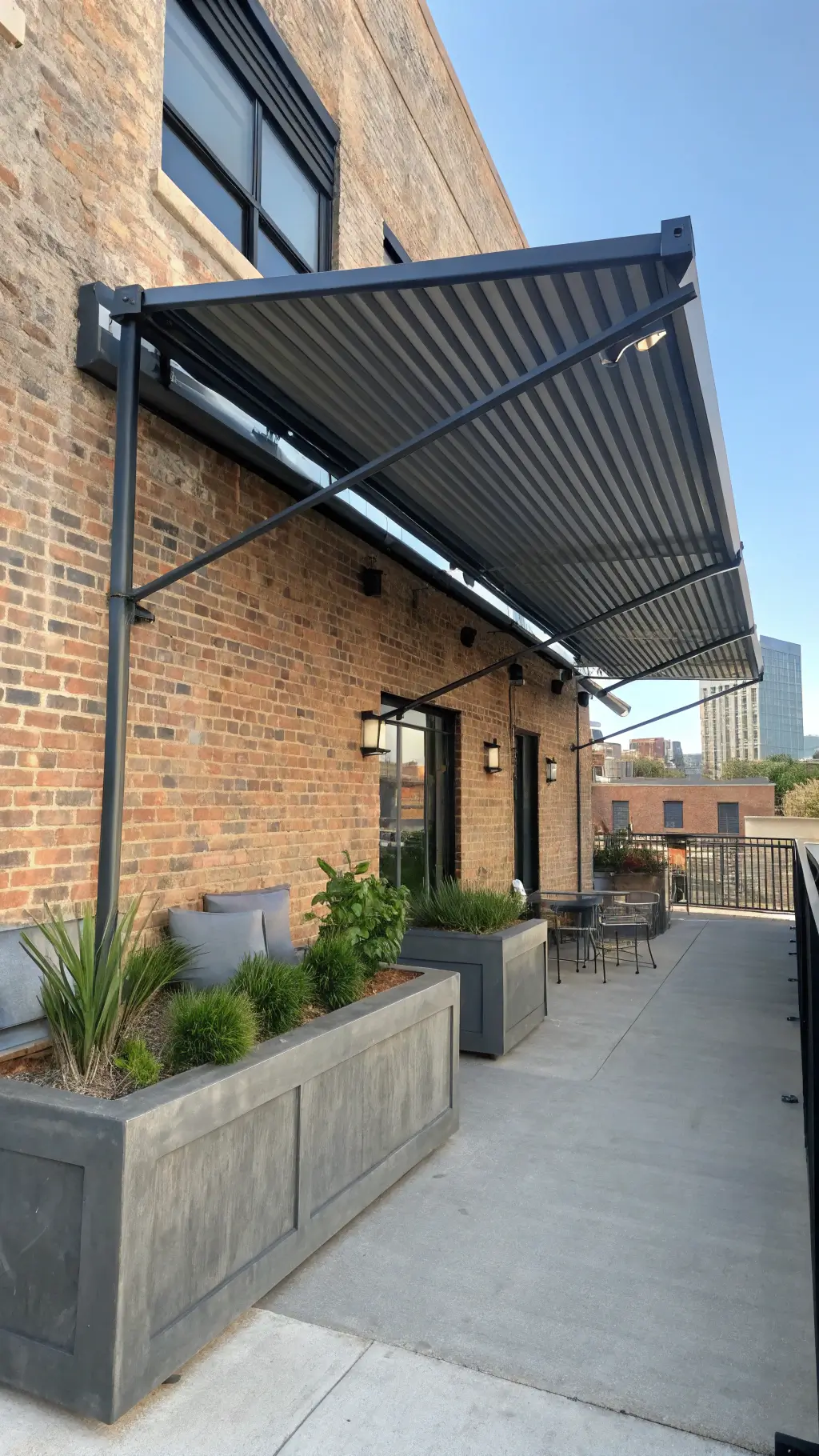 Industrial-chic urban balcony patio with corrugated metal awning, minimalist furniture, concrete planters, and early morning shadow play; cityscape in the background