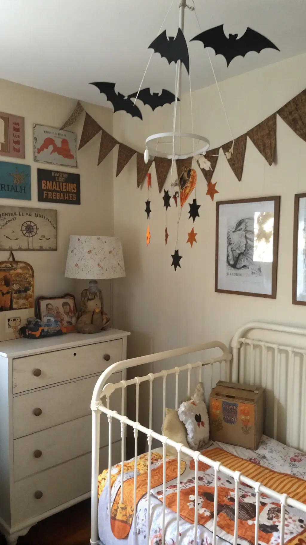 Vintage Halloween decorated children's bedroom featuring a mobile of paper mache creatures, a 1950s Halloween print quilt on a white iron bed and a distressed dresser with paper decorations.