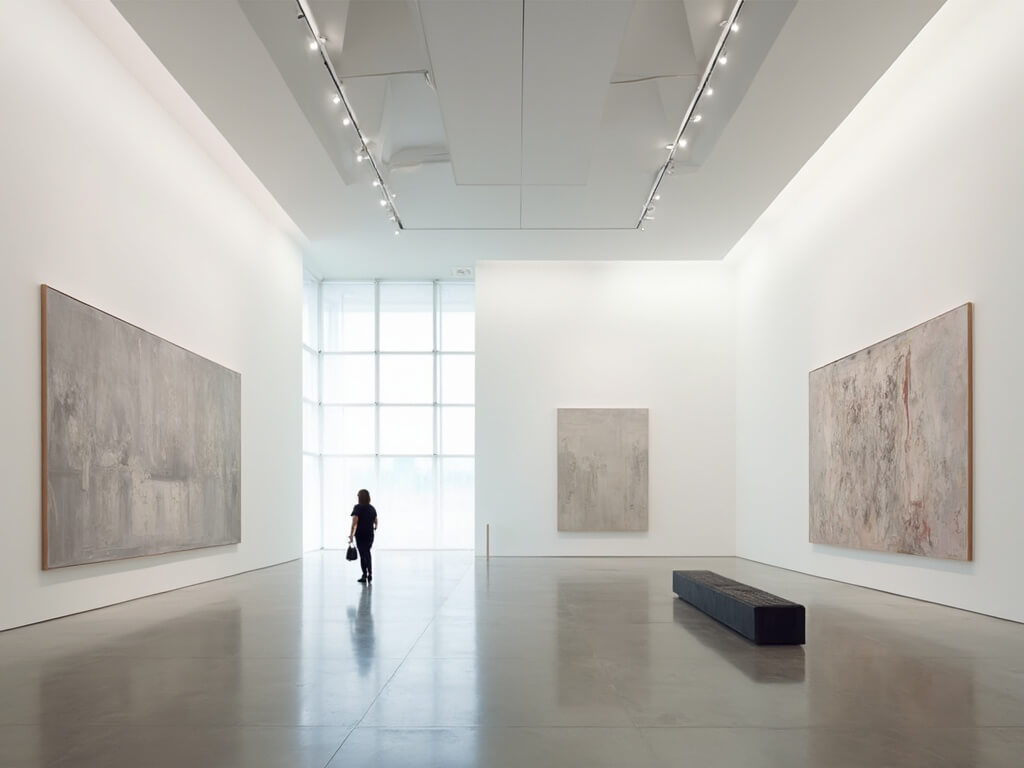 Visitor contemplating contemporary abstract paintings in the minimalist, brightly lit interior of the Kemper Museum of Contemporary Art