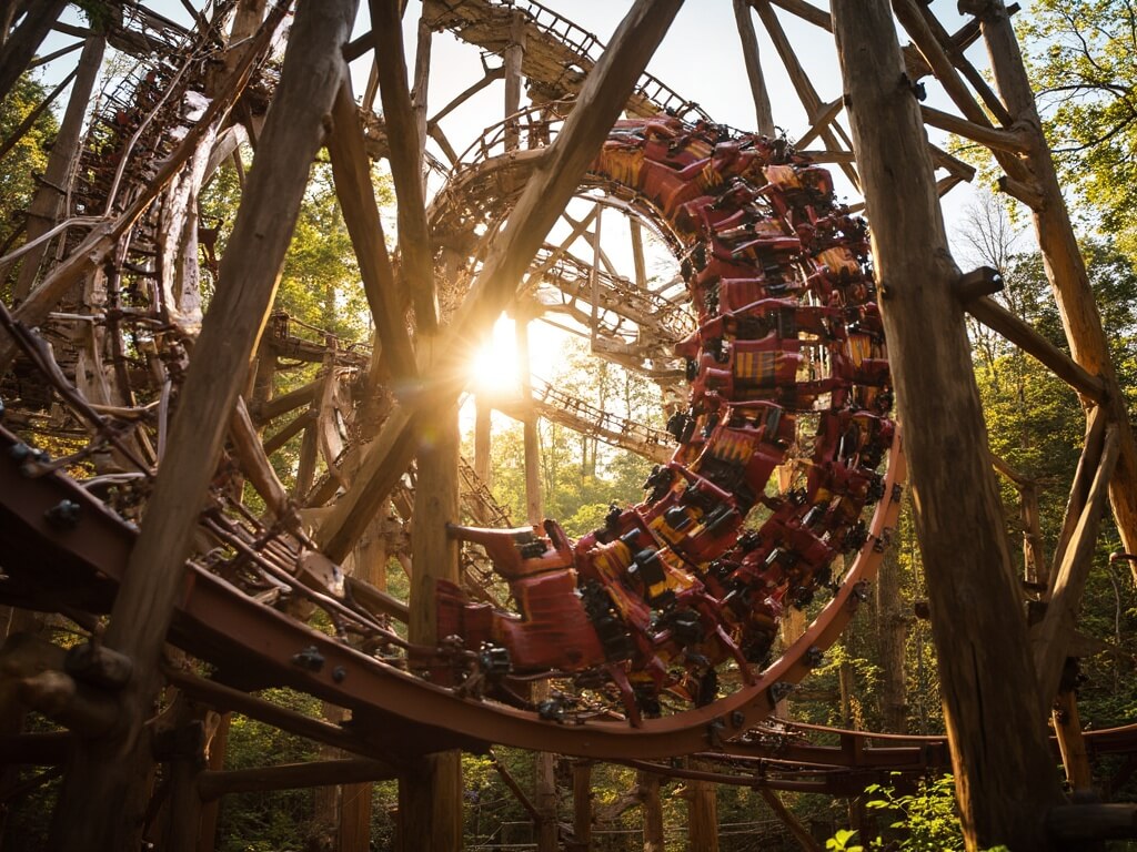 Outlaw Run wooden roller coaster at its 720-degree barrel roll, with riders inverted at peak among the wooden structure supports, in golden hour sunlight with a forest background.